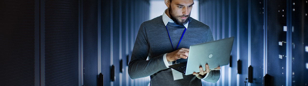 Server engineer using laptop in large data center.