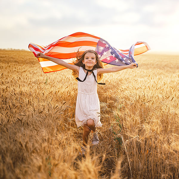 Young girl running through field with American flag