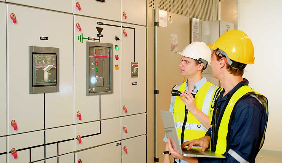 Two electricians electrical engineers in protective uniform checking voltage control panel screen system at electrical cabinet for generate electricity of factory in manufacture industrial