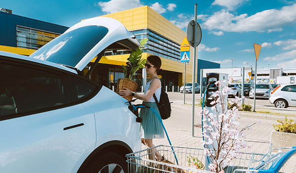 Woman charging vehicle at commercial shopping center.