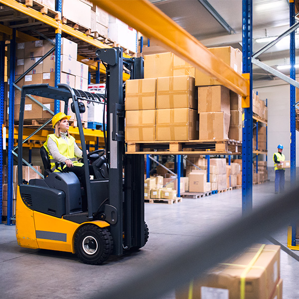 Female warehouse worker carrying boxes on forklift