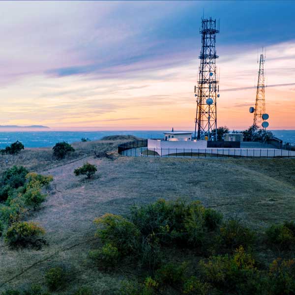 Aerial view of open rolling hills in suburban Southern California.  Radio tower atop hill during sunset surrounded by mountains and ocean