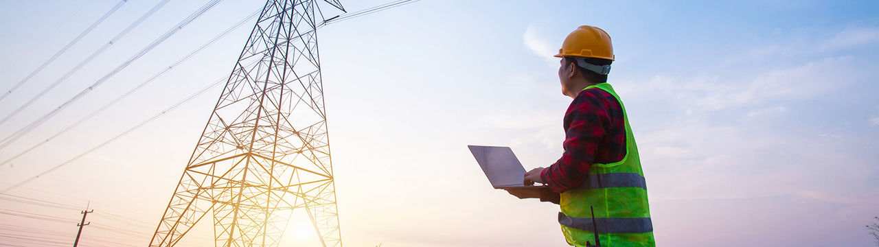 Engineer with laptop near utility tower