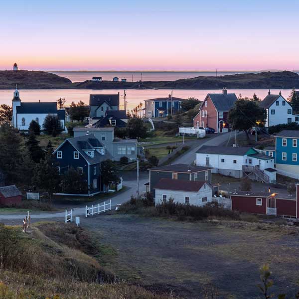 A small town by the edge of the ocean with simple houses and a church; outside lights are still on as dawn beaks, Goose Cove , Trinity, Newfoundland, Canda