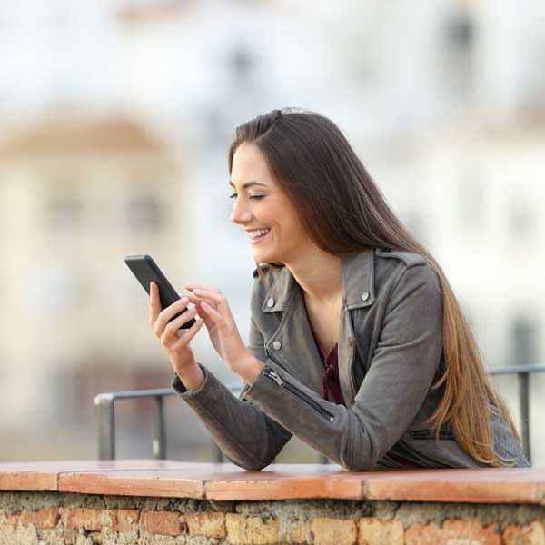 Happy girl using a smart phone in a balcony in a town