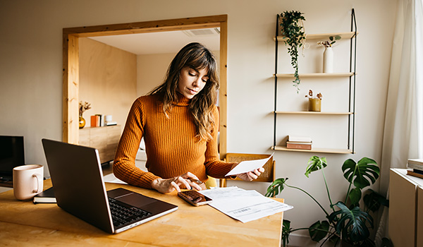 Woman managing invoices and finances at home office using laptop.