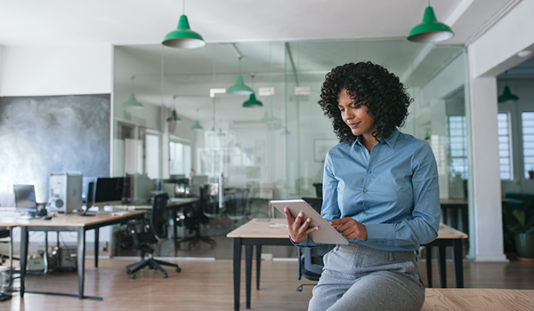Businesswoman sitting on an office table using a tablet.